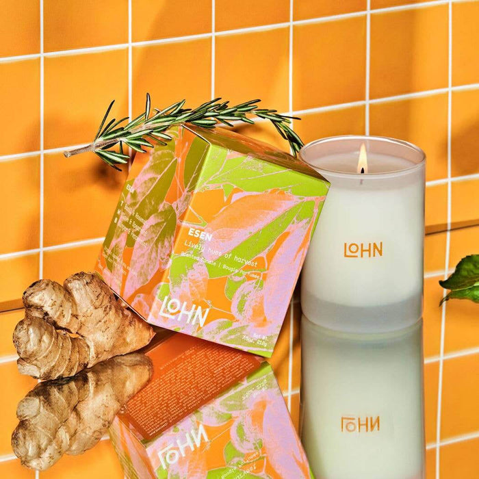 White lit candle and orange, green an dpink packaging with 'LOHN' branding on an orange tiled background