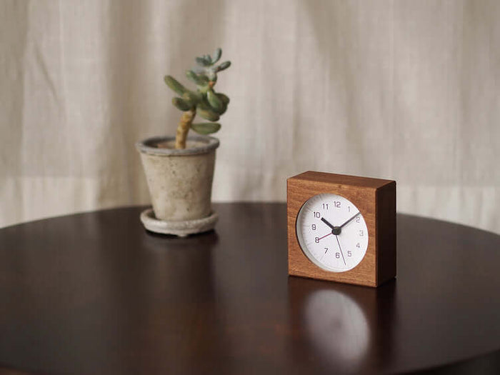 Wooden clock and potted plant on a dark surface with a neutral background