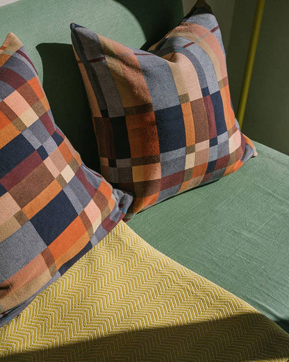 Plaid patterned pillows on a green sofa next to yellow throw.