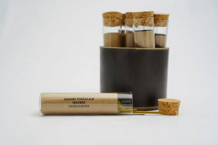 Set of tubes with cork lids in a cup and an open tube of sandalwood incense on a white background