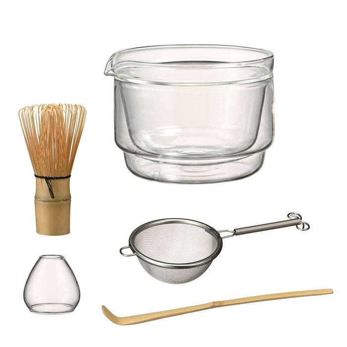 Matcha set including a whisk, glass bowl, strainer, whisk stand, and bamboo scoop on white background.