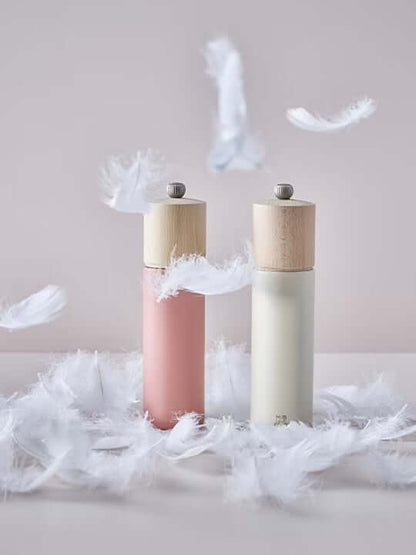 Two salt grinders in white and dark pink with wooden tops on a surface with feathers