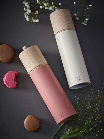 Salt and pepper grinders with wooden tops in dark pink and white laying on its side on a dark surface with cookies and flowers.