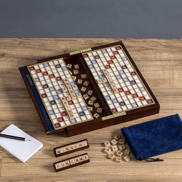 Travel Scrabble game board unfolded and open on a wooden table with tiles and pieces.