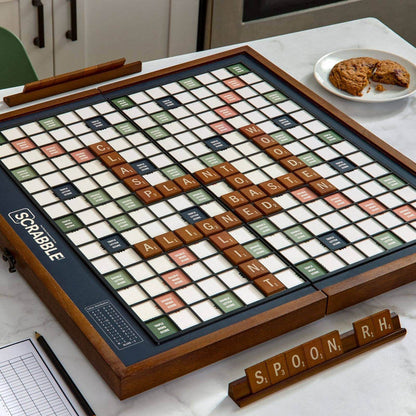 Scrabble board game on a table with tiles and a plate of cookies in the background