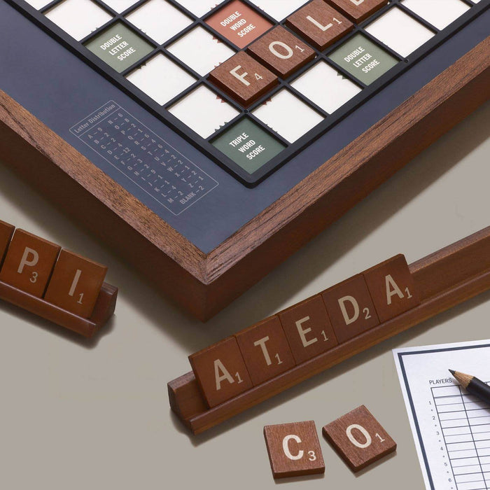 Wooden letter tiles  on racks and corner of board and scoring sheet on a beige surface.