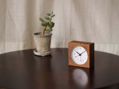 Wooden clock and potted plant on a dark surface with a neutral background